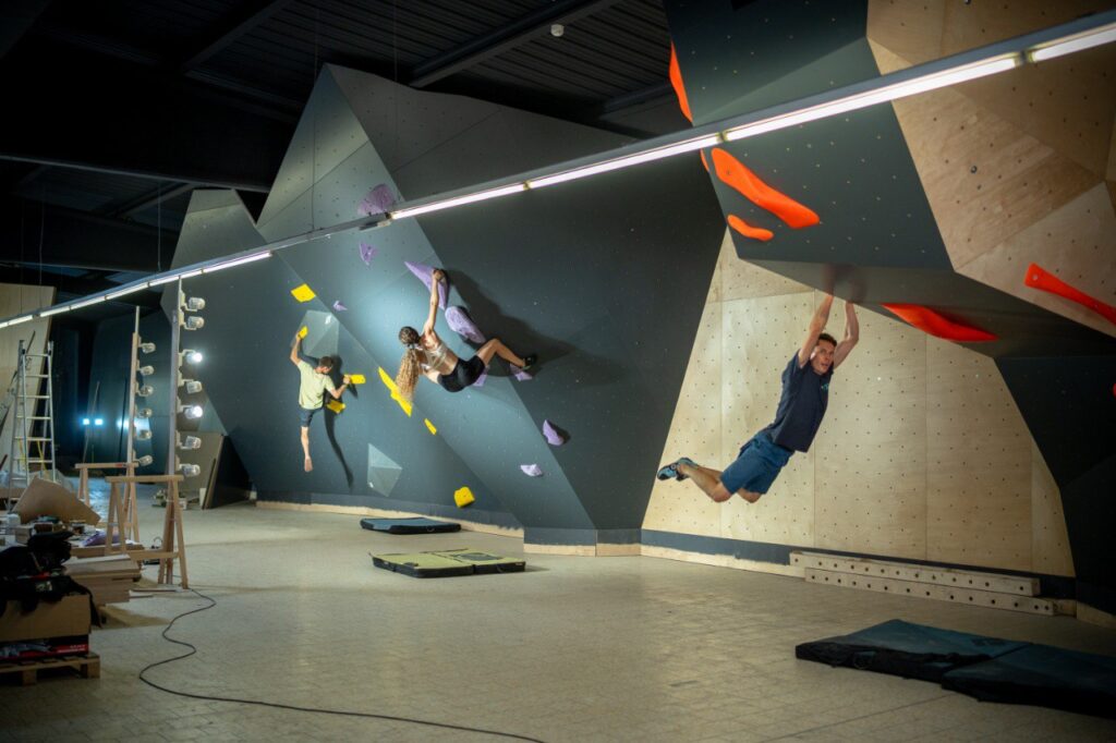 Varias personas escalando en un gimnasio de escalada con diferentes rutas